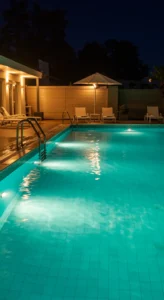 Piscina residencial iluminada à noite, com luzes subaquáticas criando reflexos na água e área de lazer ao fundo.